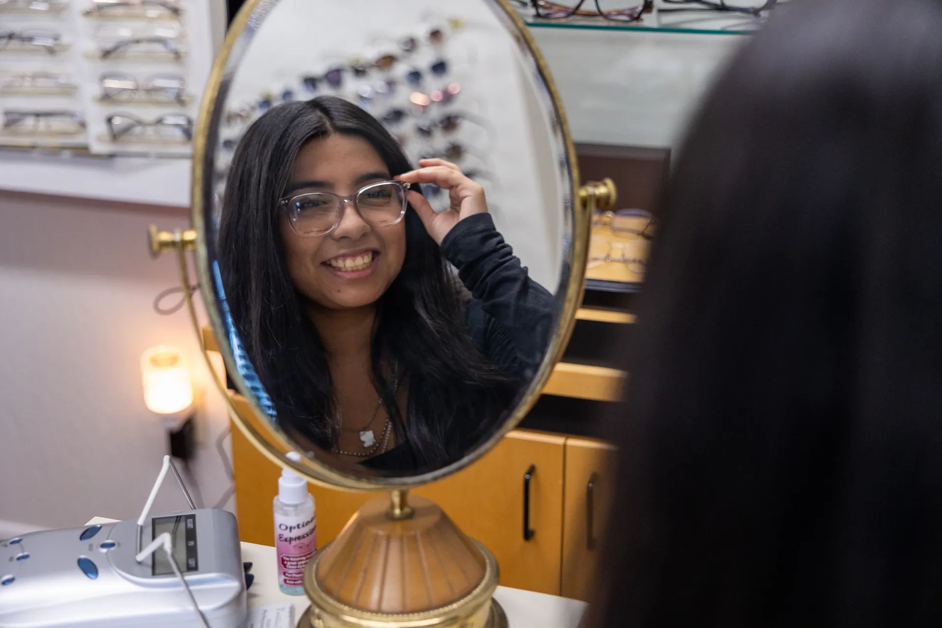 a woman wearing glasses and looking into mirror